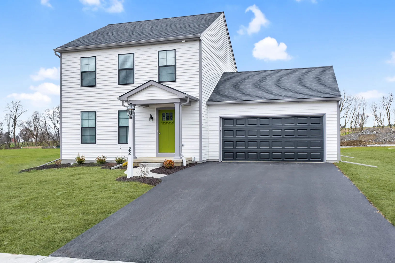 A modern two-story white house with a green front door, black shutters, and a double garage, set on a neatly manicured lawn with a paved driveway under a blue sky with scattered clouds.