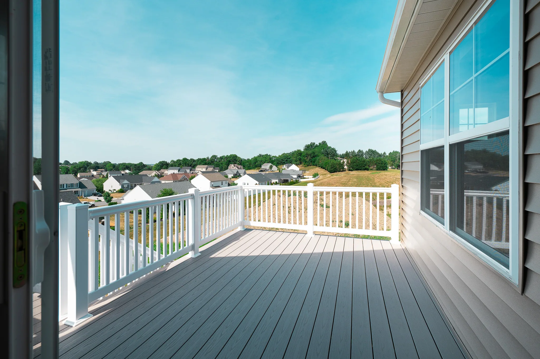 A spacious, sunlit deck with white railings offers an Eagle's View of a suburban neighborhood in Summergrove, with rows of houses and green trees under a blue sky.