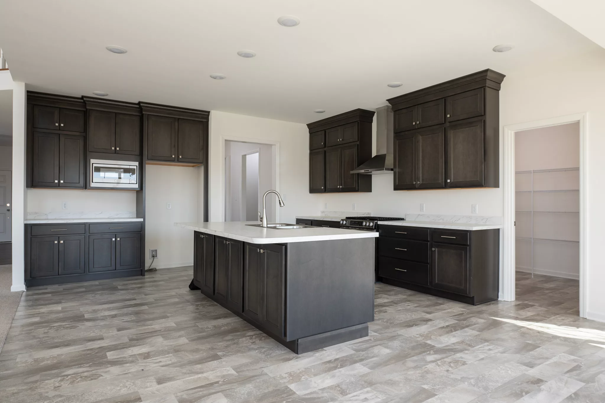 Modern Lawrenceville kitchen with dark wood cabinets, a large central island, stainless steel appliances, marble countertops, and light tile flooring. Open shelving is visible in an adjacent pantry through a doorway.