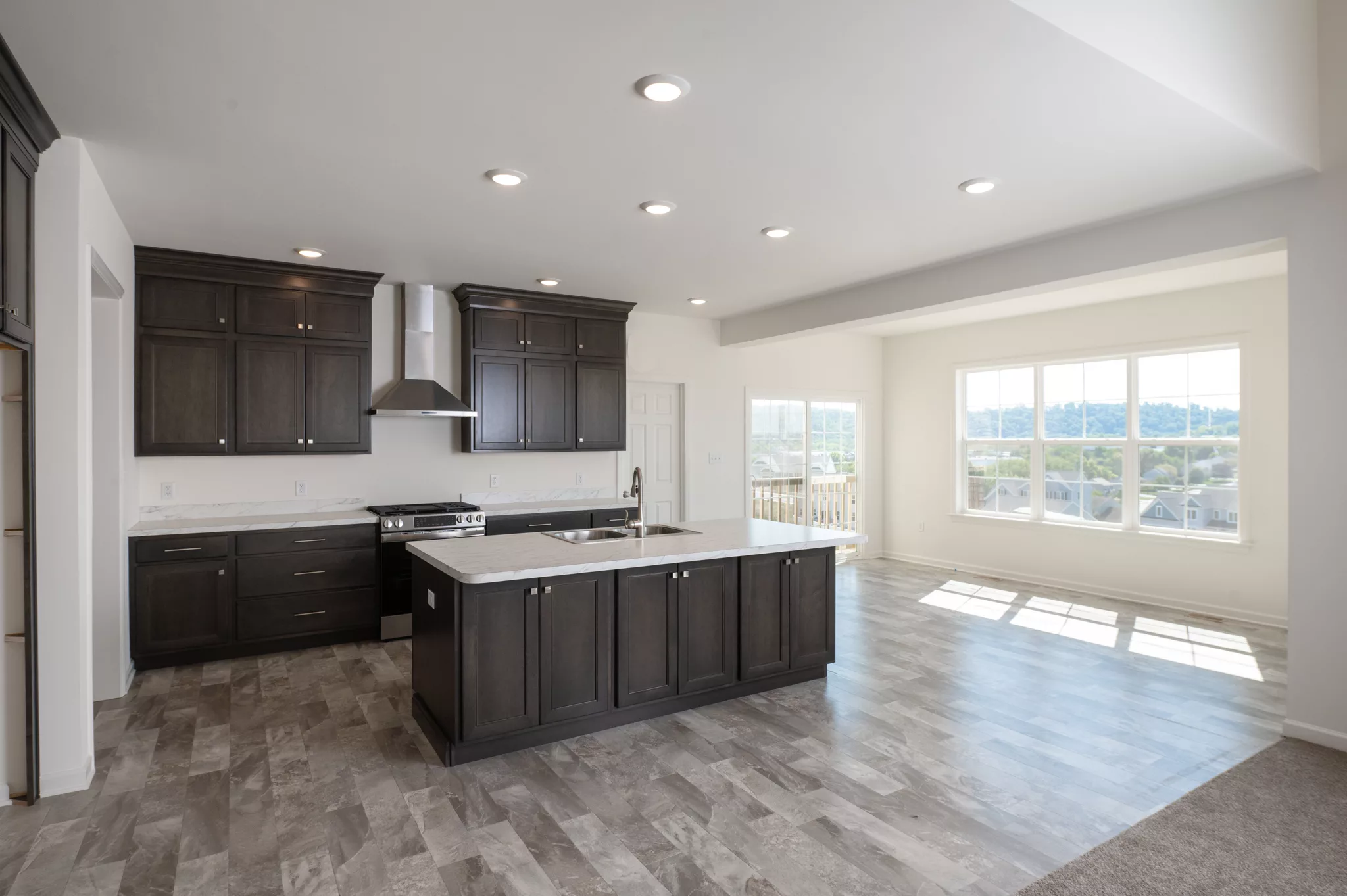 Modern Lawrenceville kitchen with dark wood cabinets, stainless steel appliances, a spacious island with sink, and open layout flowing to a bright living area featuring large windows and tile flooring.
