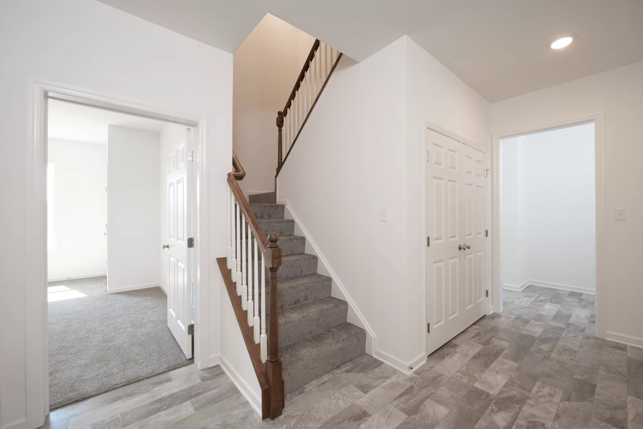 A bright, clean hallway in Lawrenceville features gray tile flooring, a carpeted staircase with a wooden handrail, white walls, and doors leading to carpeted rooms.