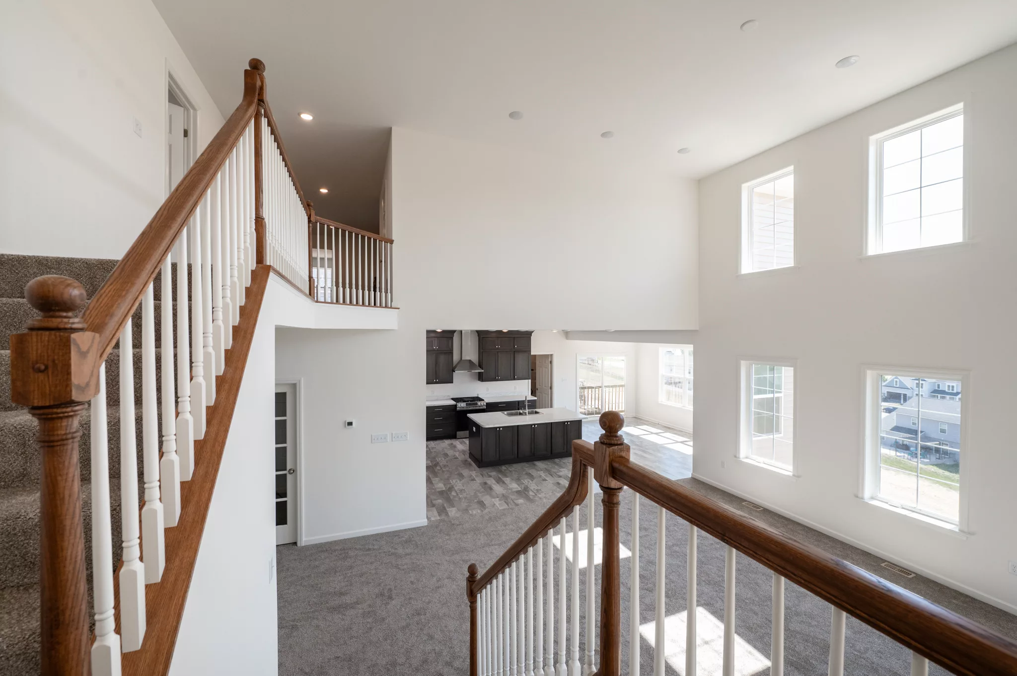 View from a staircase inside a bright, modern Lawrenceville home with large windows, carpeted floors, white walls, and an open-concept kitchen and living area featuring dark wood cabinets and abundant natural light.