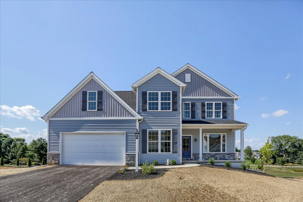 A modern two-story blue house with white trim, a double garage, large windows, and a covered front porch, set against a clear blue sky with minimal landscaping and paved driveway.