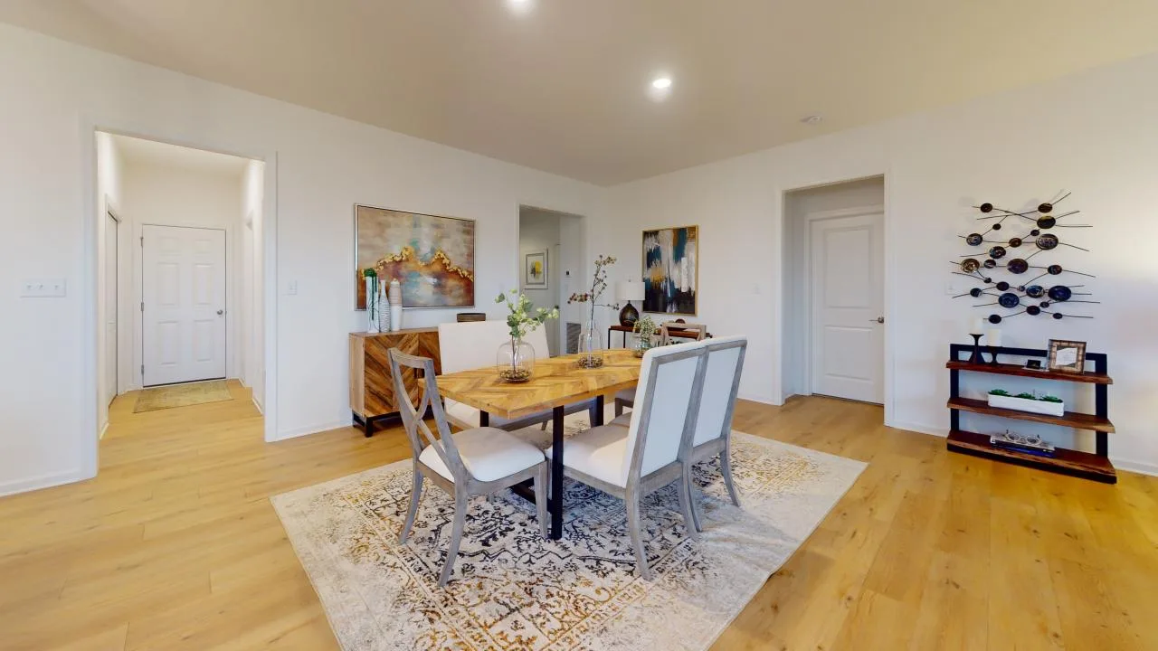A modern dining area featuring a wooden table with chairs, stylish décor, and an elegant rug on warm wooden flooring.