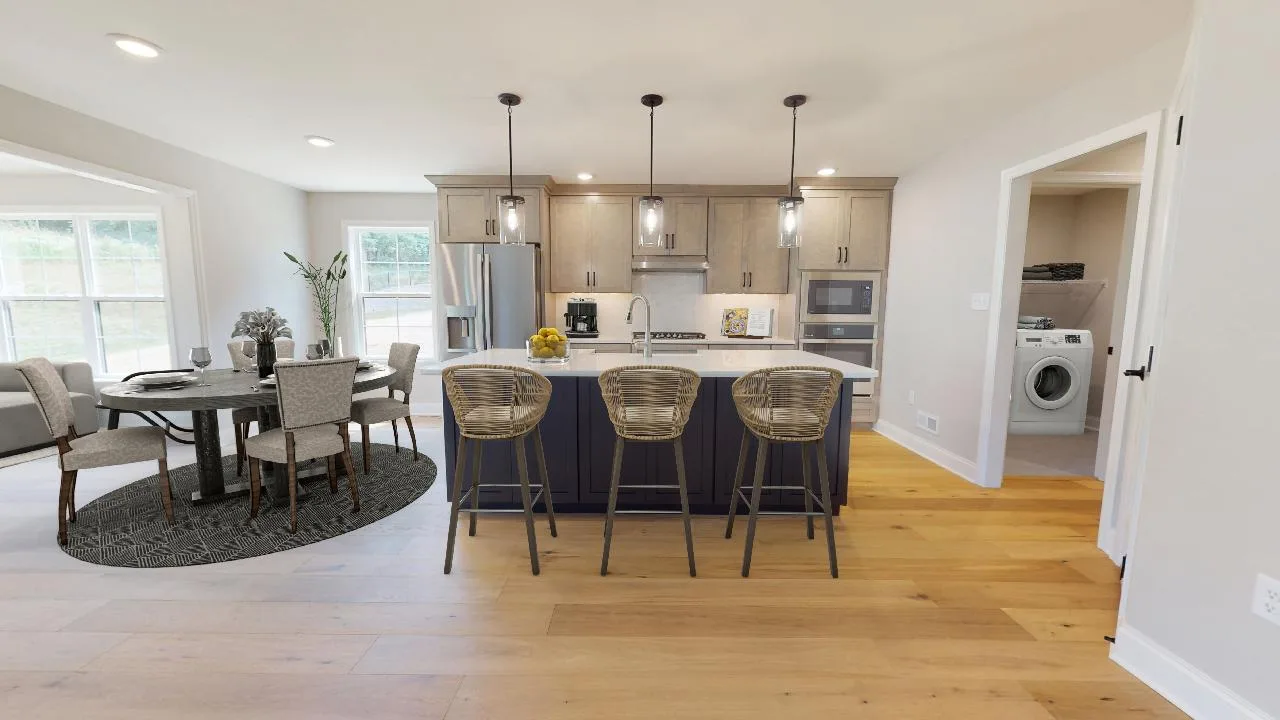 Modern kitchen with a central island and three wicker bar stools, adjacent to a dining area with a round table and four chairs. A laundry room with washer and dryer is visible through an open door.
