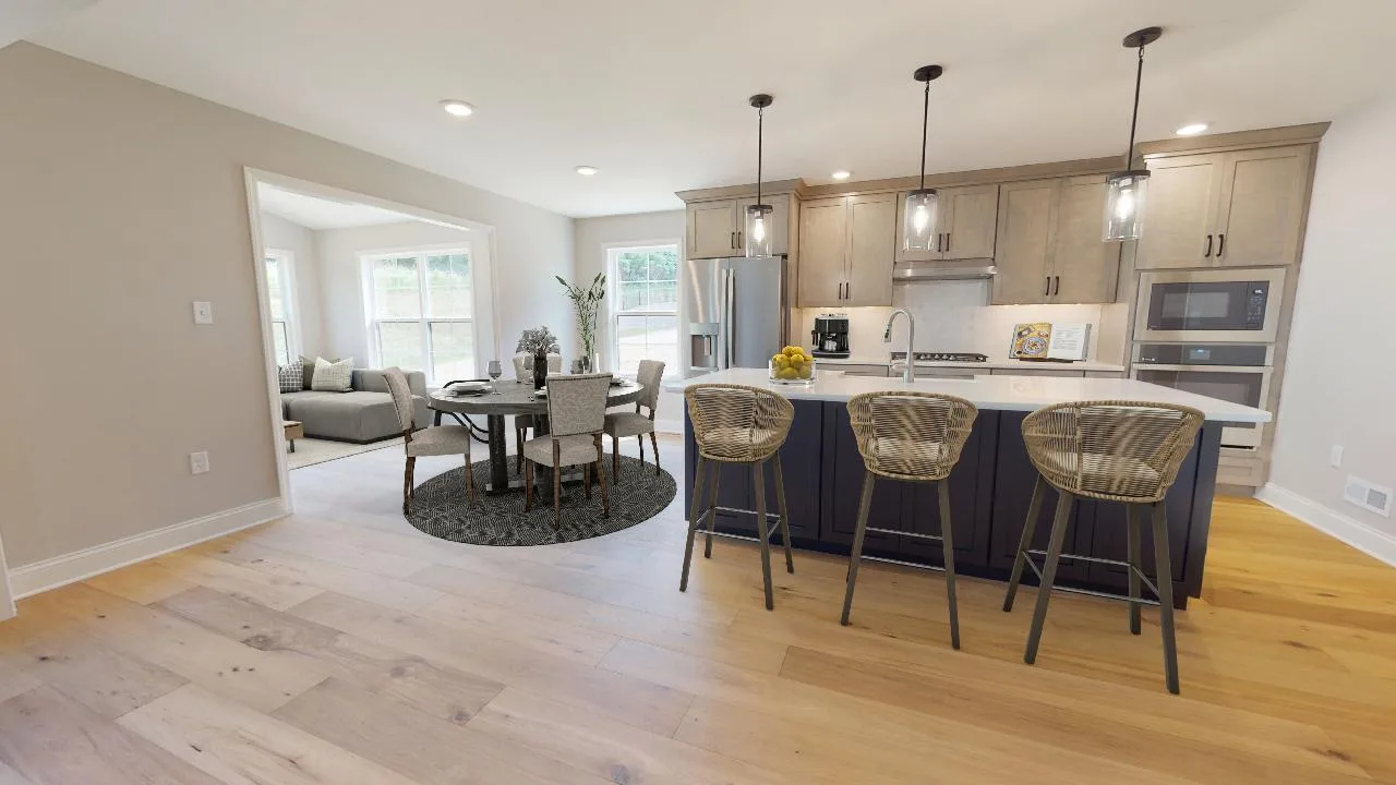 Modern kitchen and dining area with wooden floors, an island with three wicker stools, pendant lights, stainless steel appliances, and a round dining table with four chairs near large windows.
