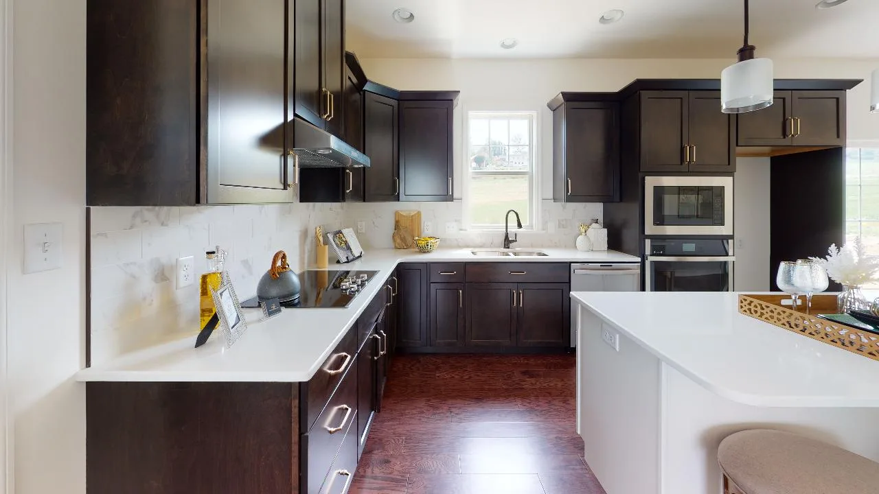 Modern kitchen with dark wood cabinets, white countertops, stainless steel appliances, a gas stove, island with barstool seating, and a window above the sink allowing natural light to fill the space.