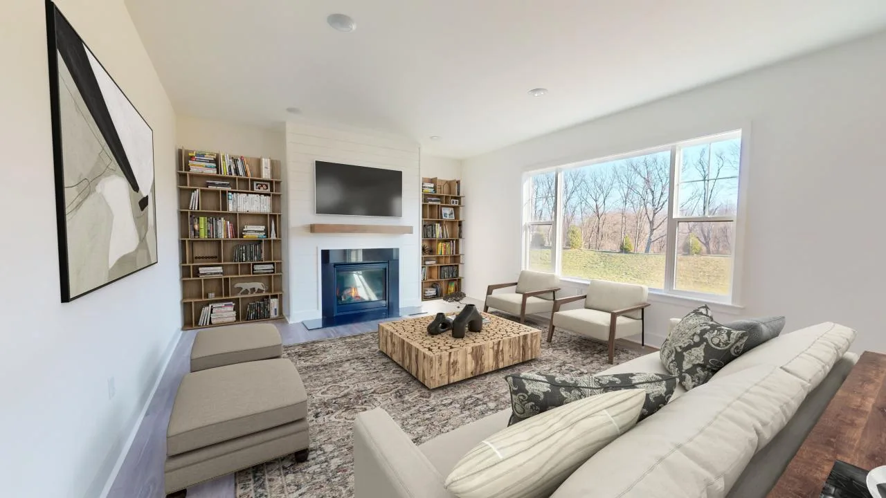A bright living room with large windows, a sofa, two armchairs, a patterned rug, a wooden coffee table, a fireplace with a TV above it, built-in bookshelves, and abstract wall art.