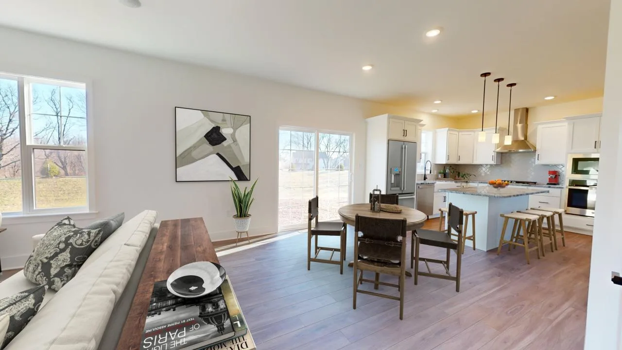 A bright, modern open-concept living space with a couch, wooden dining table, kitchen island with stools, white cabinets, and large windows letting in natural light.