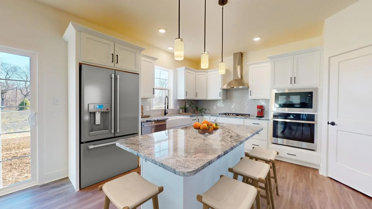 A modern kitchen with white cabinets, stainless steel appliances, an island with a gray marble countertop, four wooden stools, and pendant lights. Sunlight streams in from a glass sliding door on the left.