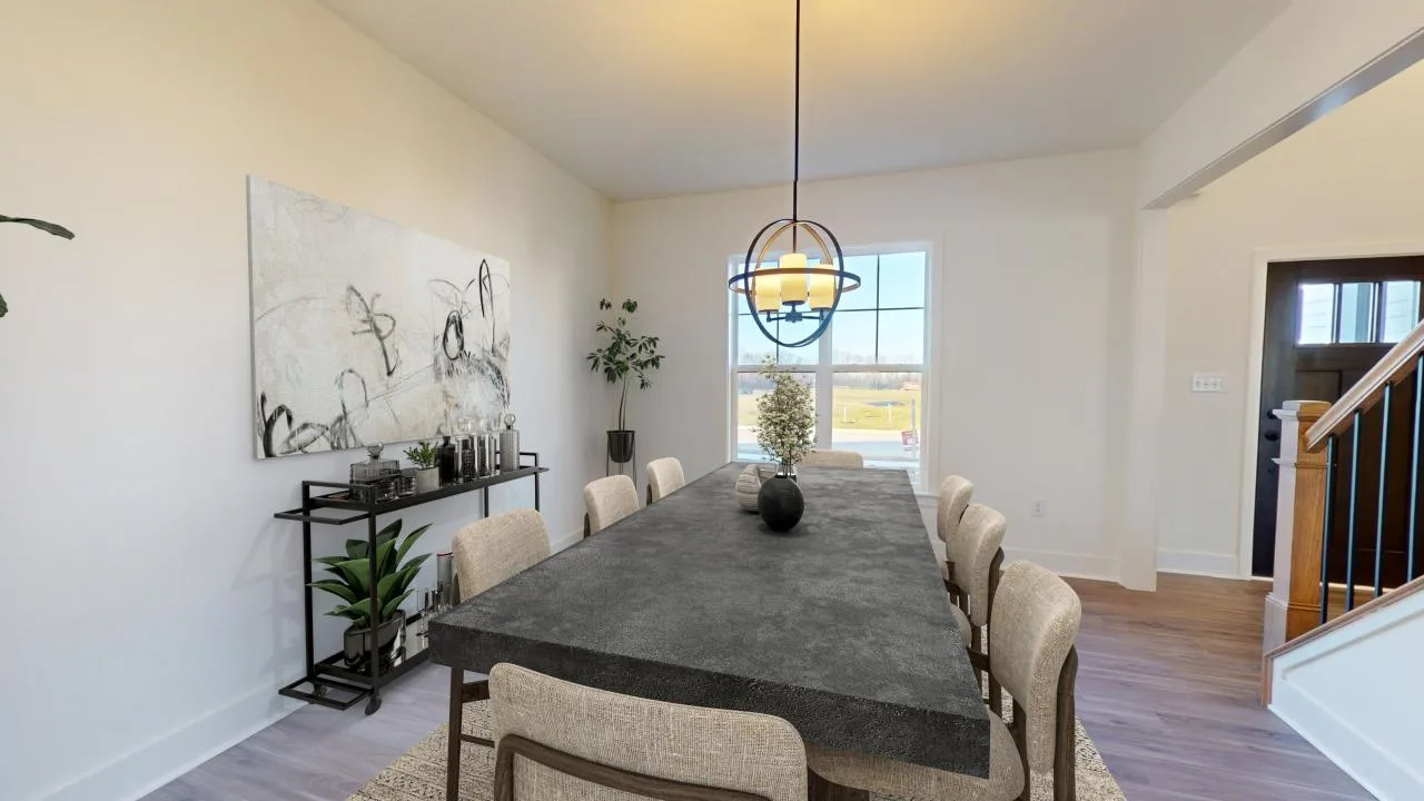 Modern dining room with a long dark rectangular table, eight beige chairs, a pendant light above, abstract wall art, plants, and a window letting in natural light. Stairs and a hallway are visible to the right.