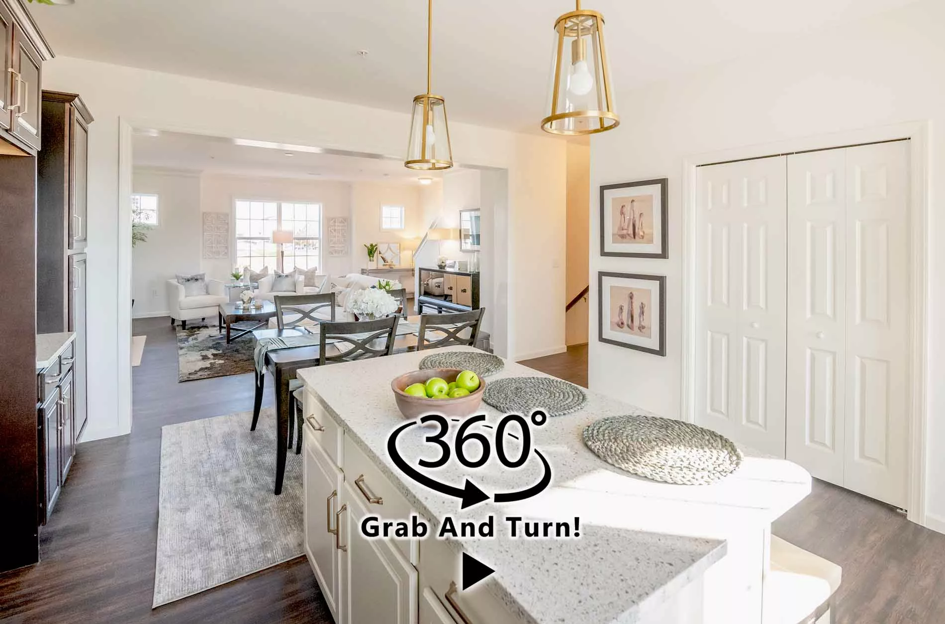 Bright, modern kitchen with white cabinets, an island, pendant lights, and a bowl of green apples. Open layout leads to a living room with large windows. “360° Grab And Turn!” text overlays the image.