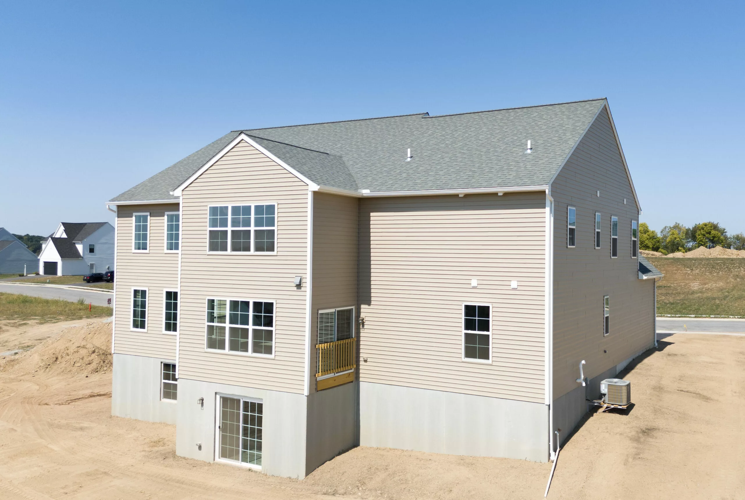 A newly constructed beige two-story house in Lawrenceville, featuring large windows, a small balcony, and a gray shingle roof, surrounded by bare earth and no landscaping.