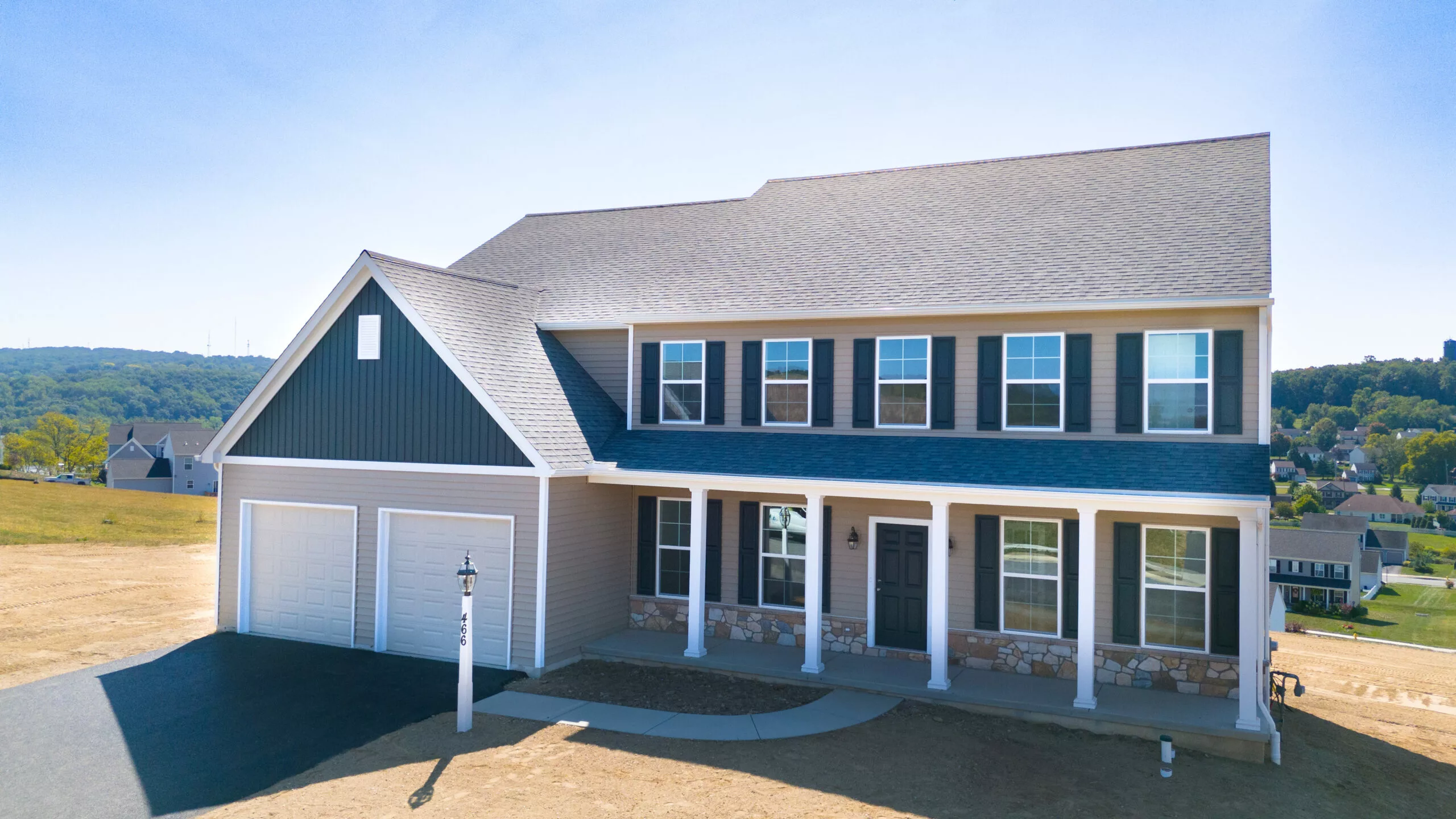 A newly built two-story suburban house in Lawrenceville with gray siding, white trim, a covered front porch, double garage, and a paved driveway, set on a grassy lot under a clear blue sky.