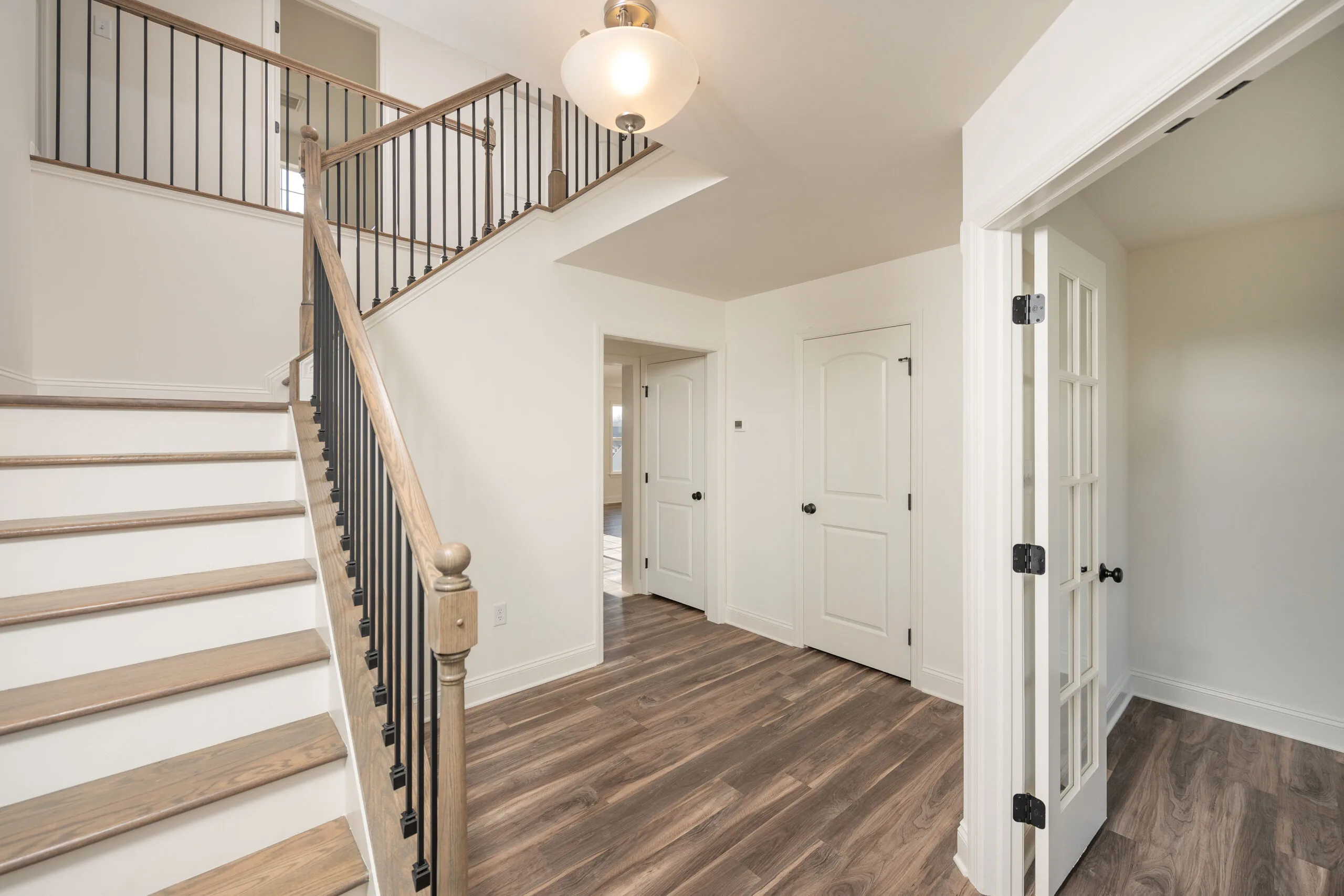 Bright entryway in a modern home featuring wood-style flooring, a staircase with wooden handrails and black spindles, white walls, and multiple doors including French doors to the right.
