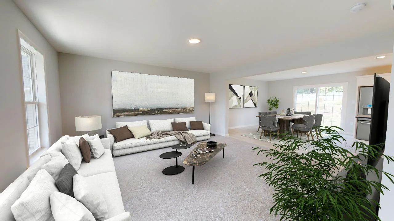 A bright, modern living room with a white sofa, neutral décor, two round coffee tables, a large plant, and a dining area with a table and chairs near windows letting in natural light.