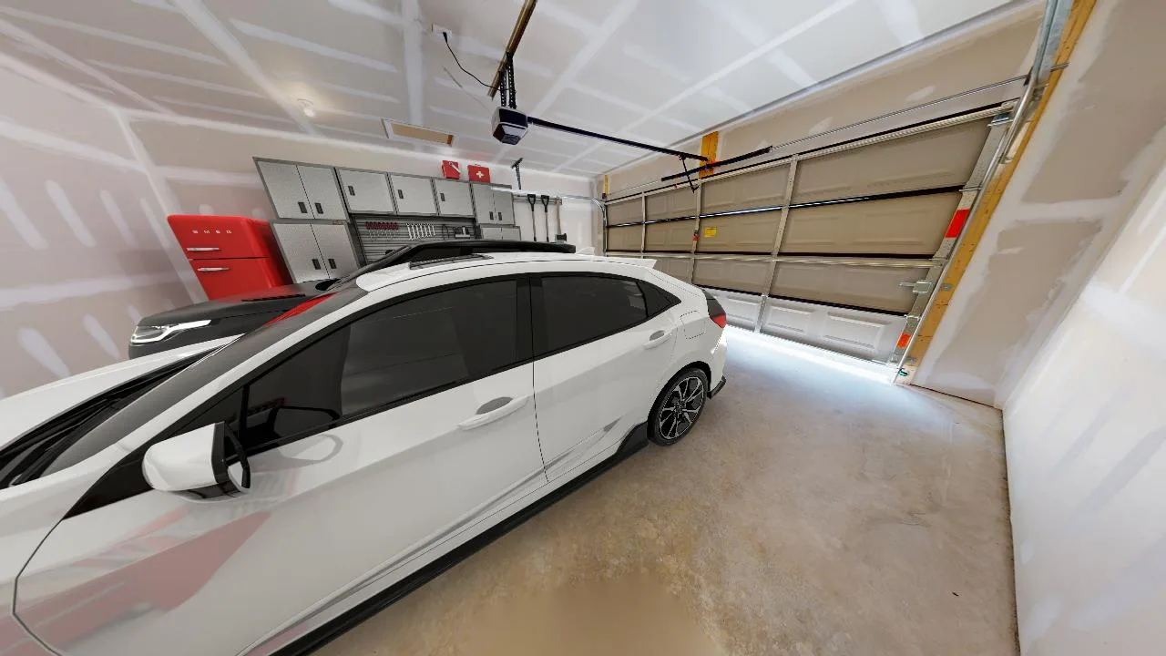 A white car is parked inside a clean, unfinished garage with beige walls, overhead storage cabinets, a red tool chest, and a closed garage door.