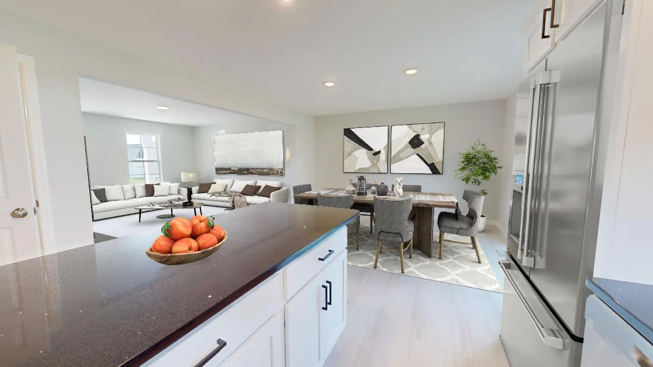 View from a modern kitchen island with a bowl of tomatoes, overlooking an open dining area with a set table and a living room featuring a couch, large artwork, and a potted plant by the window.
