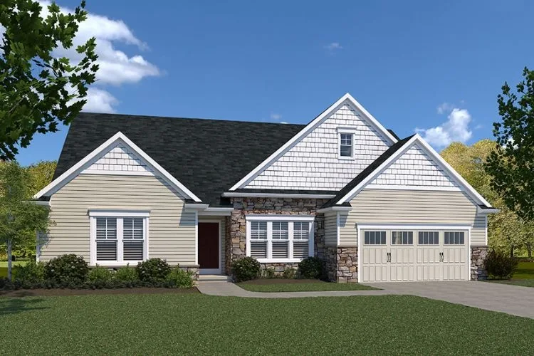 Single-story suburban house with beige siding, white trim, stone accents, and a dark gray roof. It has a double garage, white shutters, and landscaped bushes along the front. The sky is clear and blue.