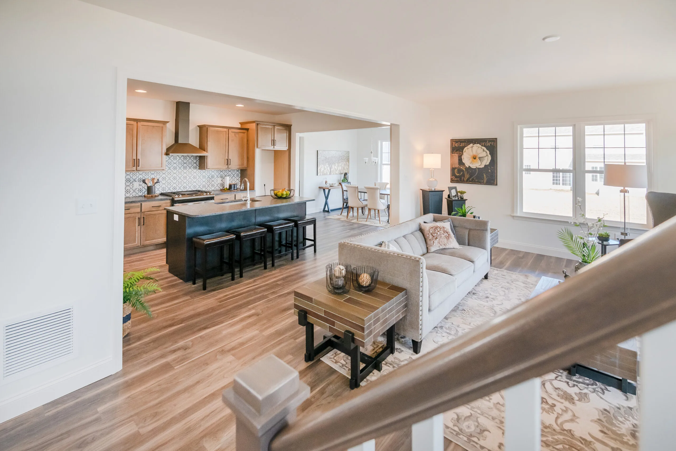 Bright open-concept living area with a modern kitchen, dining space, and cozy living room featuring neutral tones, wooden floors, a large island, and natural light from multiple windows.