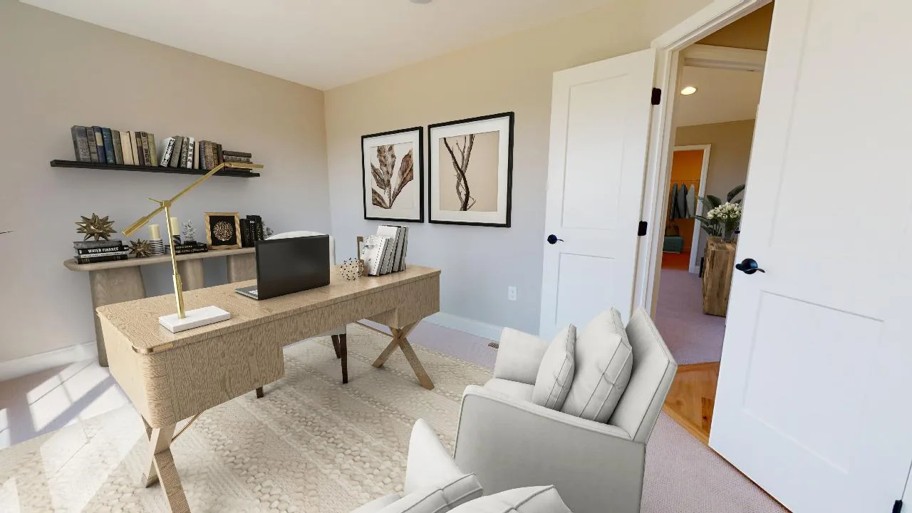 A modern home office with a wooden desk, laptop, and books. An armchair sits in front of the desk. A shelf with decor and books is against one wall, and two framed botanical prints hang above it. The room is bright with neutral tones.
