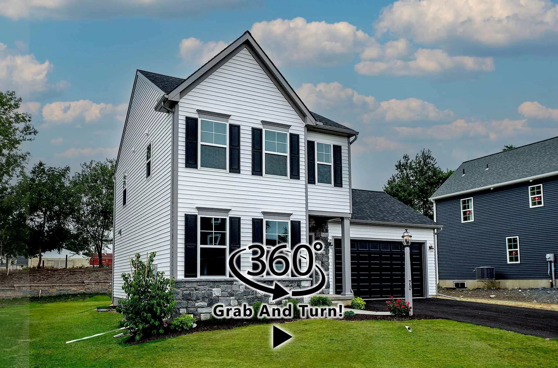 Two-story white house with black shutters and a stone foundation, a green lawn in front, and a driveway leading to a black garage. 360° Grab And Turn! text and icon are overlaid on the image.