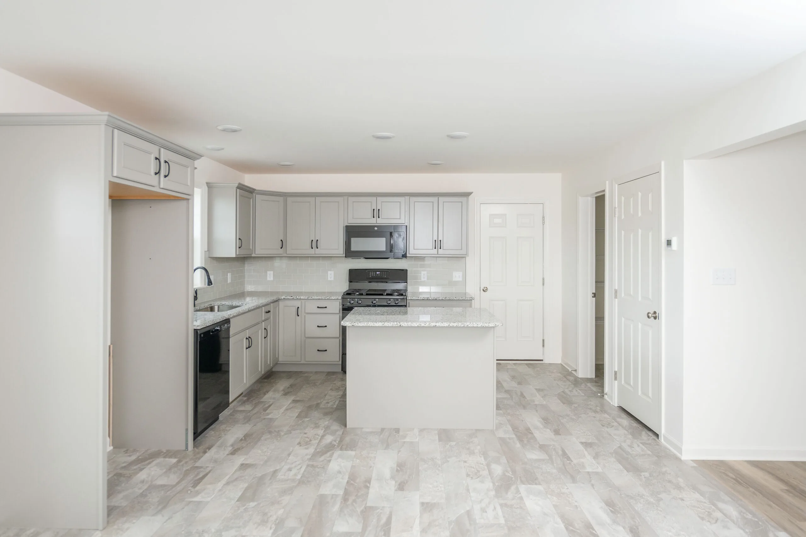Modern kitchen with gray cabinets, granite countertop island, stainless steel appliances, light-colored tile flooring, and white walls. The room is well-lit with natural light from an unseen window.