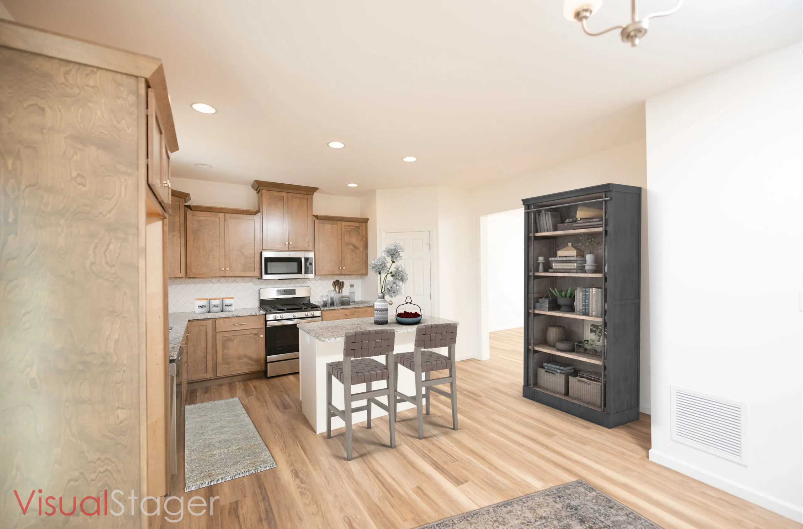 A modern kitchen with wooden cabinets, stainless steel appliances, a white island with two chairs, a gray bookshelf, and light wood flooring. A vase with flowers sits on the island.