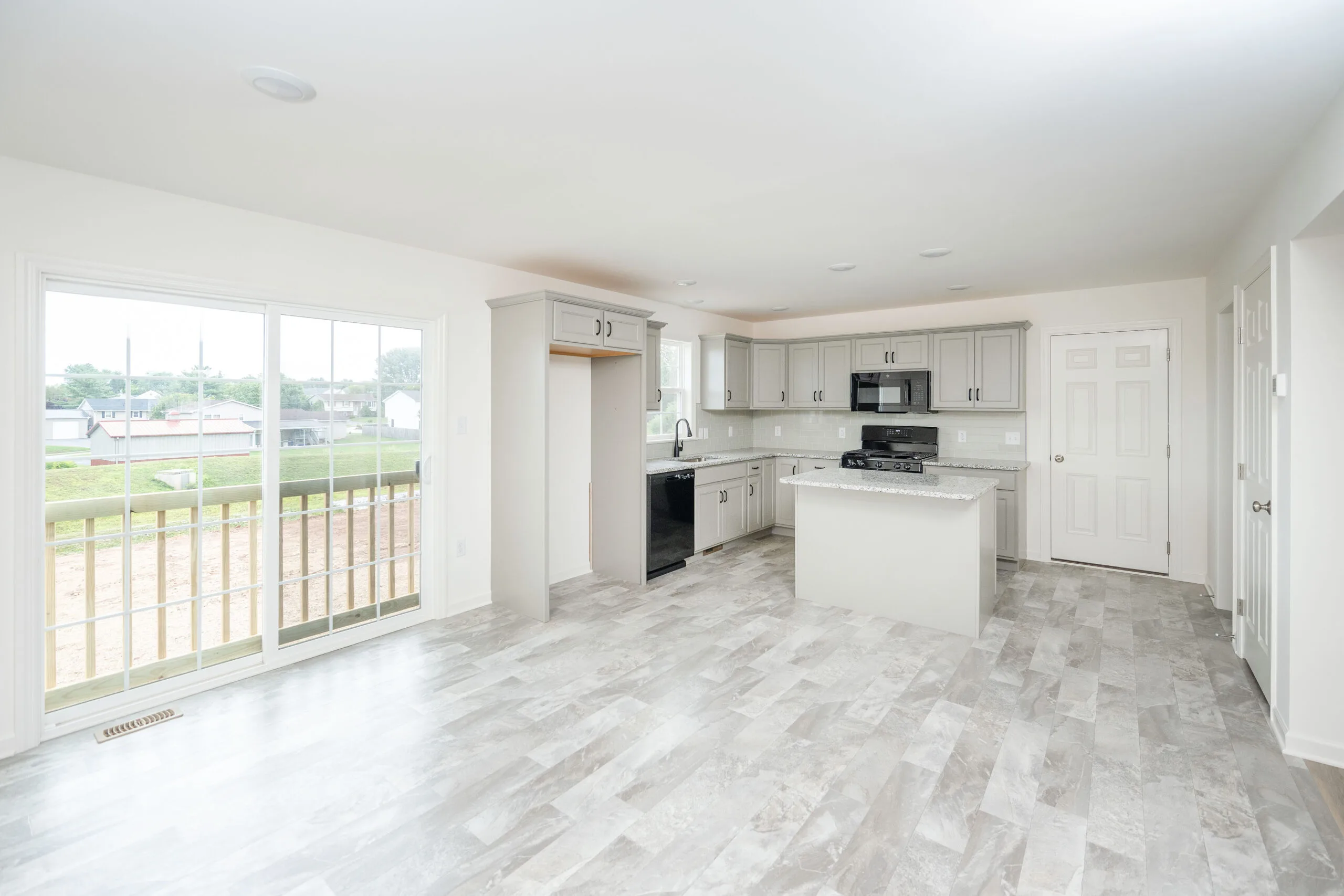 Bright, modern kitchen with gray cabinets, white countertops, stainless steel appliances, island, and sliding glass doors leading to a balcony. Light gray tile flooring throughout.