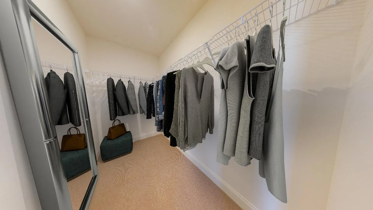 A walk-in closet with wire shelves holding neatly hung gray and black clothes, a large mirror on the left, and two bags and a green storage box on the floor at the back.