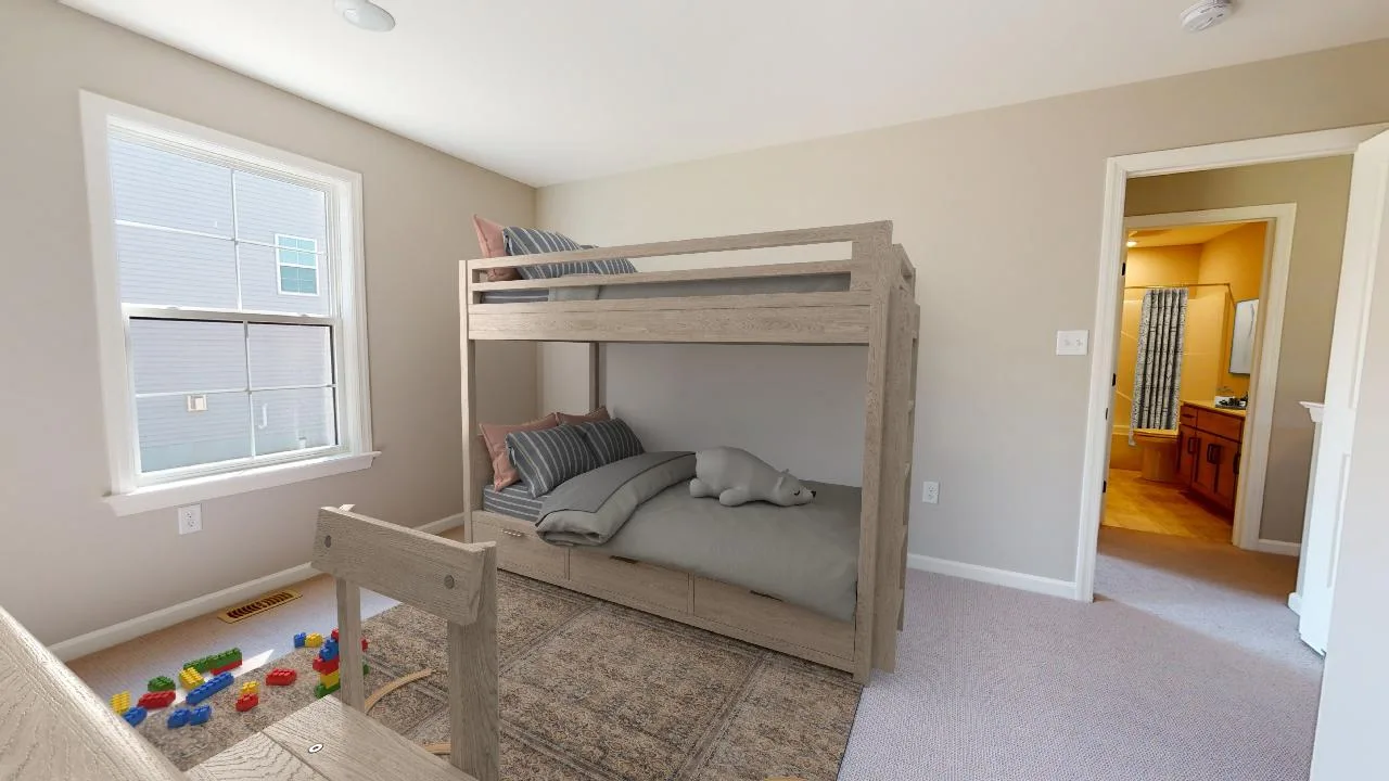 A cozy bedroom with beige walls featuring a wooden bunk bed, gray bedding, stuffed animal, toy blocks on the floor, a window letting in daylight, and an open door leading to a bathroom.