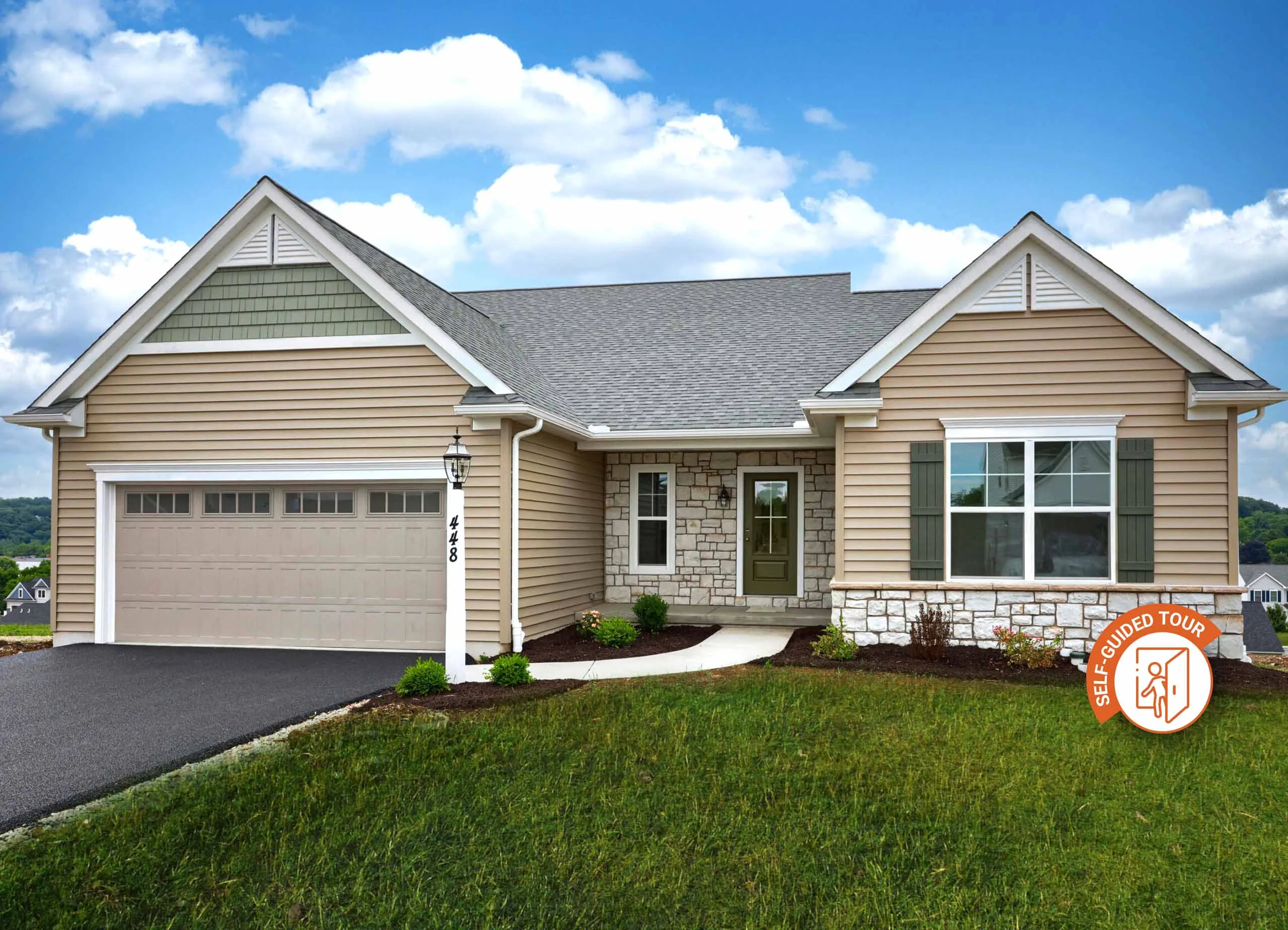 Single-story suburban house in Summergrove with beige siding, stone accents, gray shingle roof, two-car garage, front lawn, and a self-guided tour logo in the bottom right corner. Blue sky with clouds frames this American Eagle's View home.